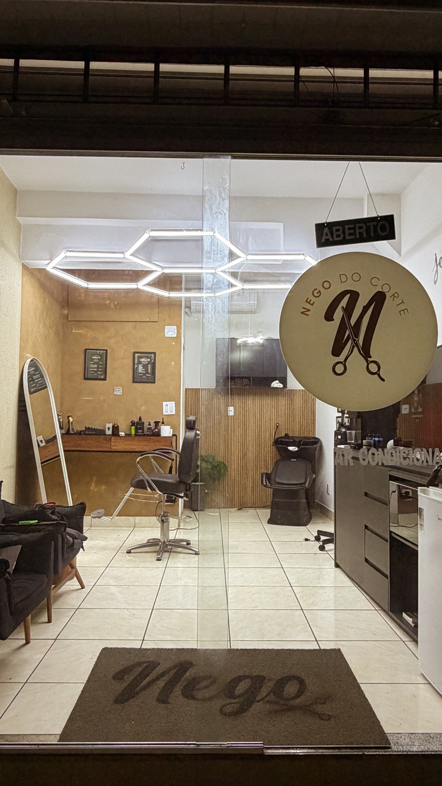 Entrada da Nego do Corte vista pela porta de vidro, com o interior da barbearia e o logotipo na fachada